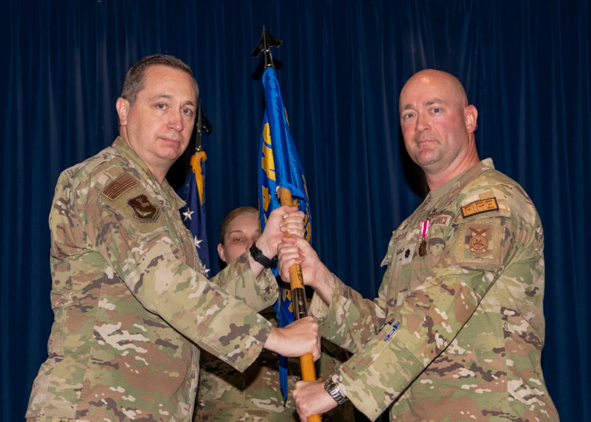 Two military men hold a guidon in between each other.