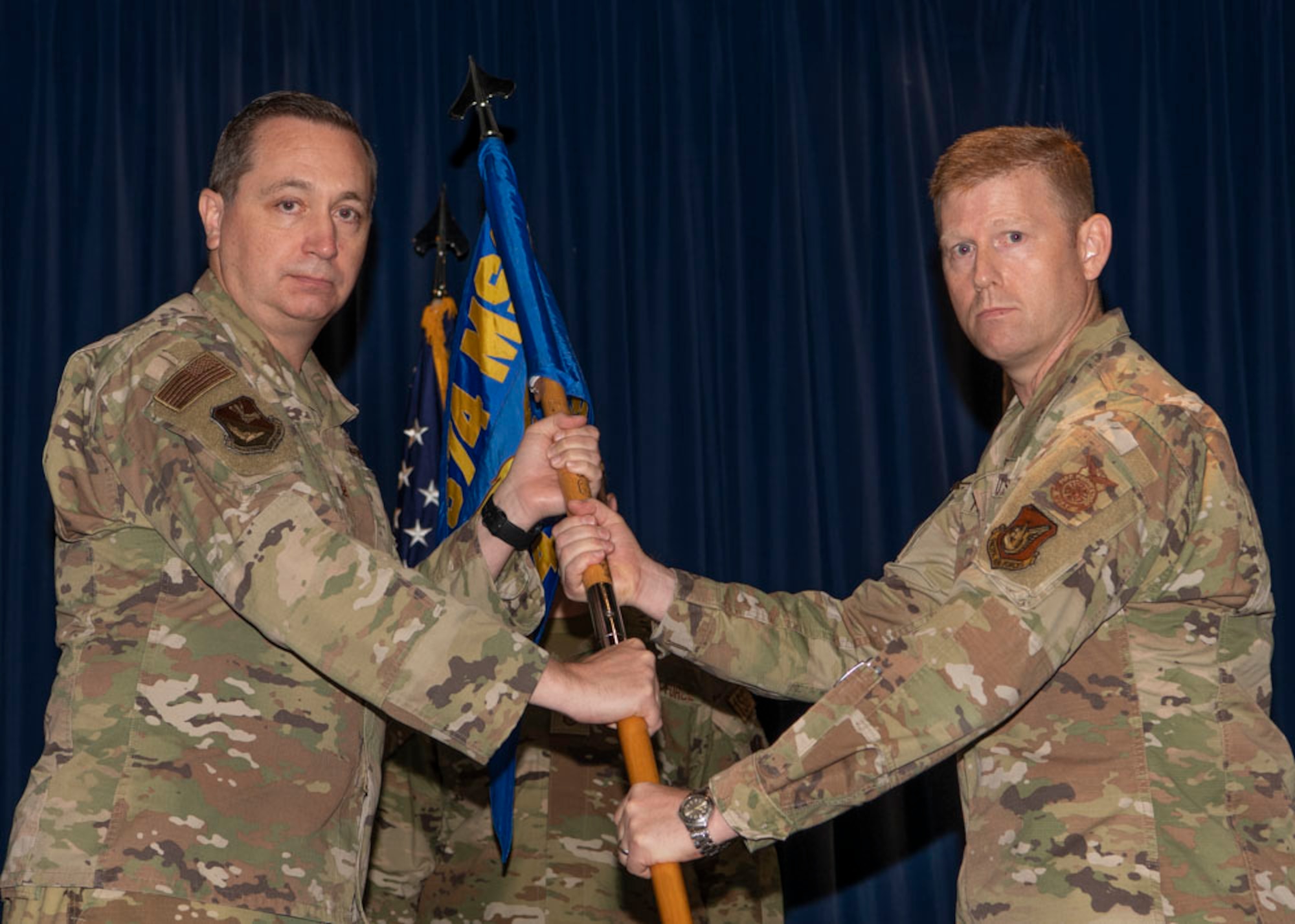 Two military men hold a guidon in between each other.