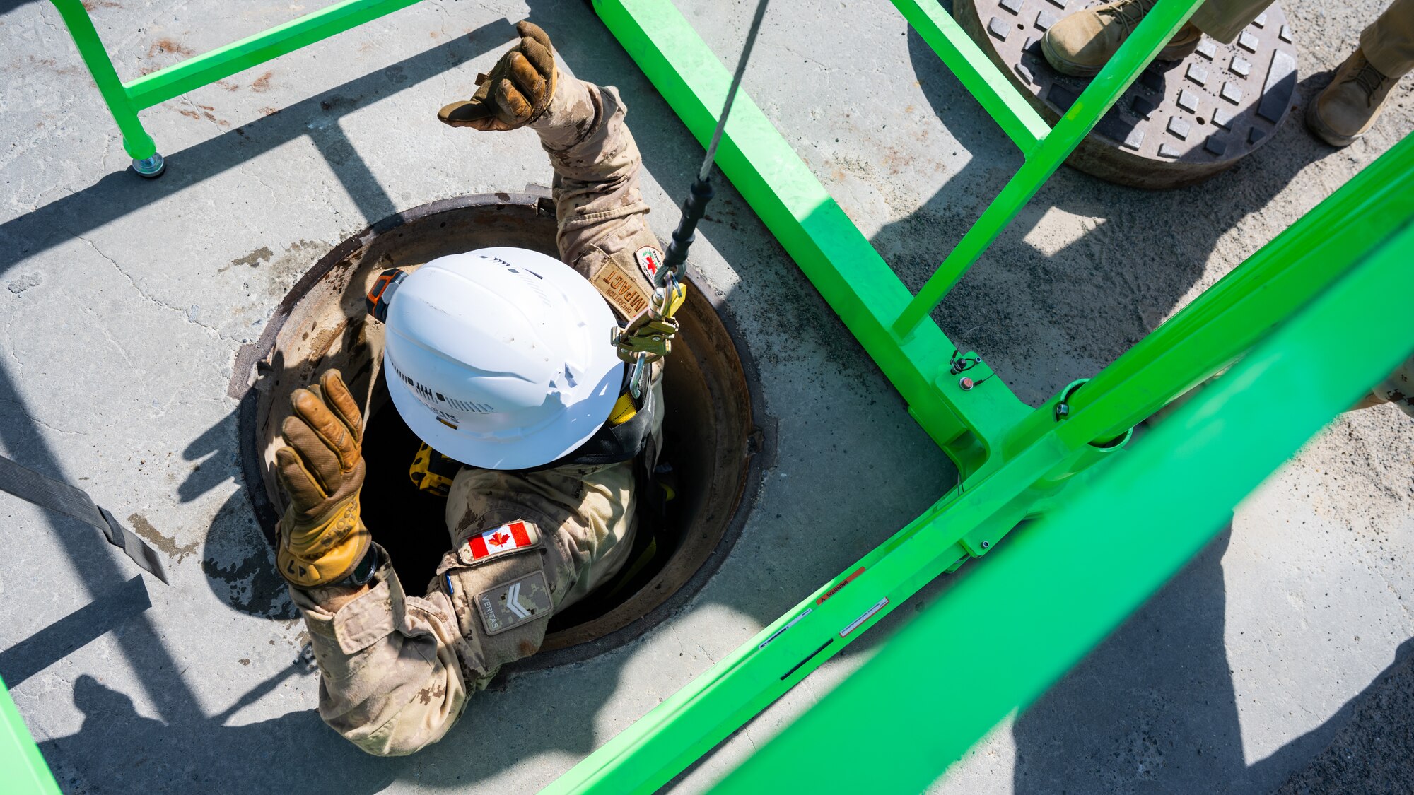 A Canadian armed forces member is hoisted up from a manhole during confined-space training at Ali Al Salem Air Base, Kuwait, July 25, 2023. This confined-space training allowed for the U.S. and our Canadian partners to share their knowledge and expertise, thus reducing the risks associated with confined-space operations for all. (U.S. Air Force photo by Staff Sgt. Kevin Long)