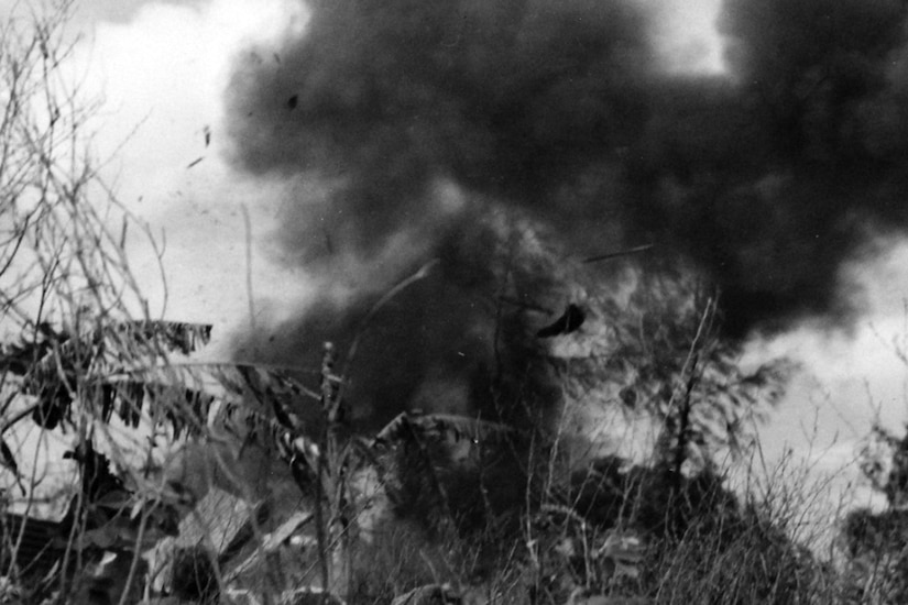 An explosion blows smoke and ash into the air. A helmet can be seen in the sky.