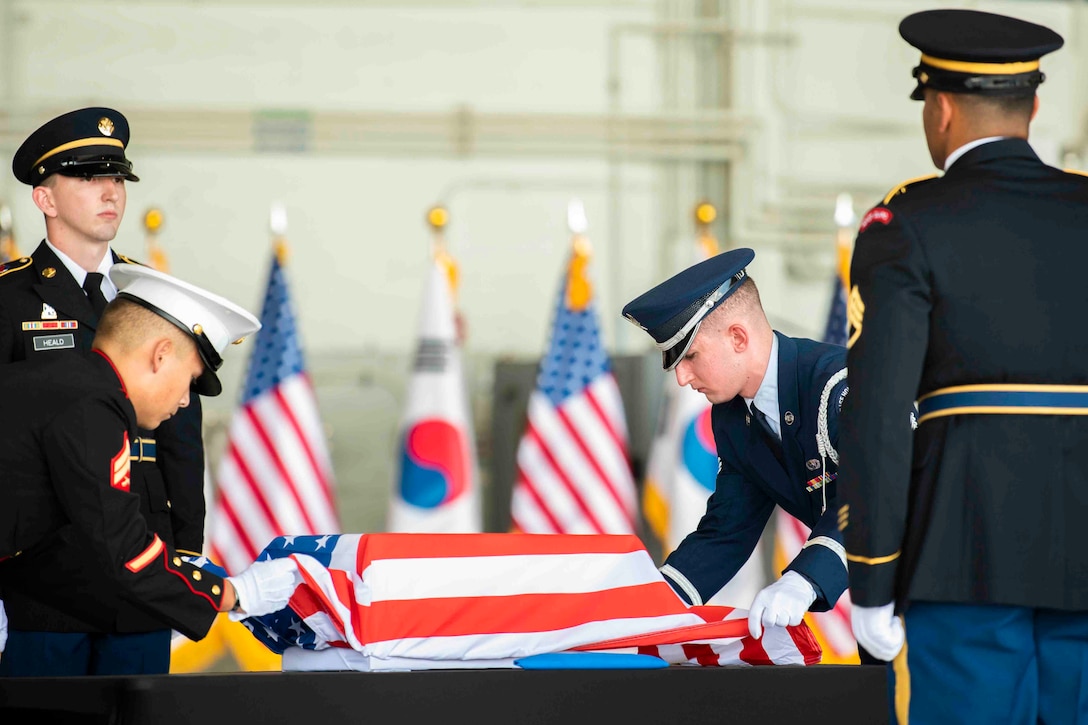 Two service members remove an American flag from a case as two others stand in formation.