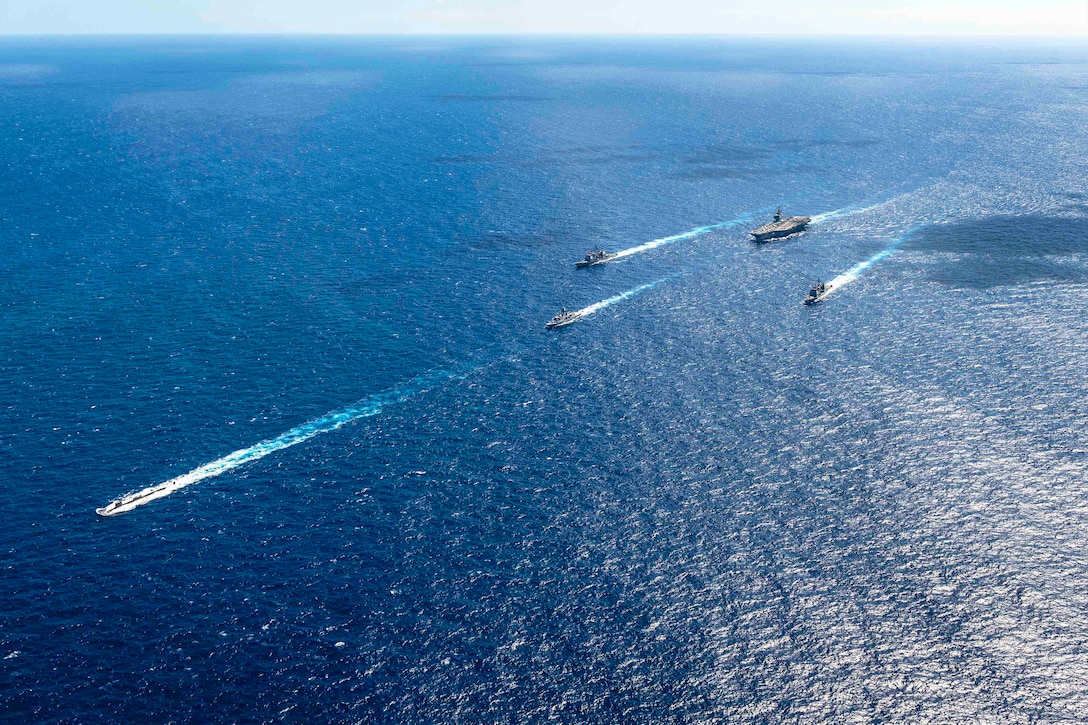 Five ships travel through a body of water in formation.