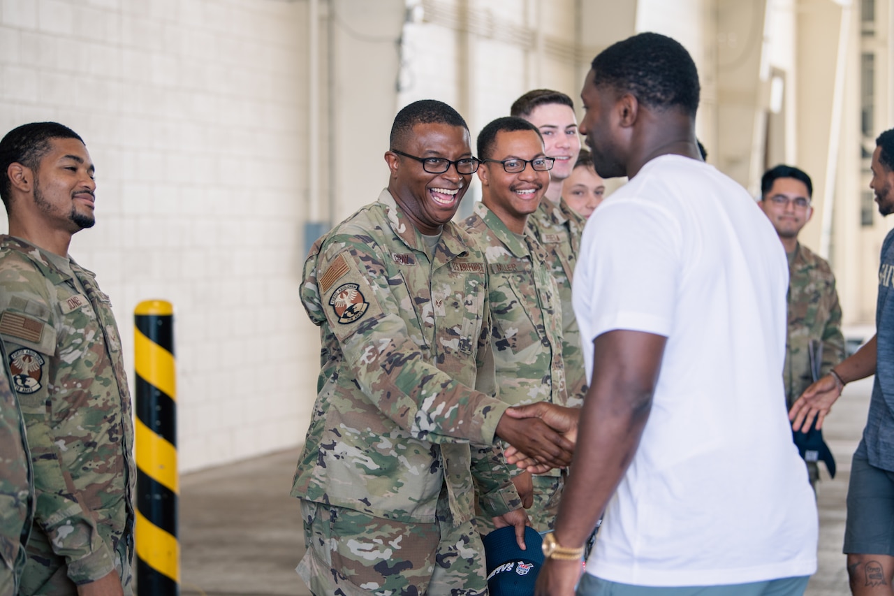 A man in uniform smiles as he shakes another man’s hand. Others beside him watch.