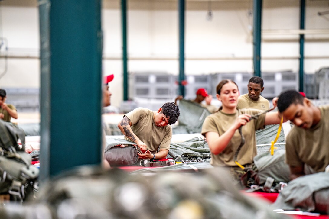 Soldiers pack parachutes in bags.