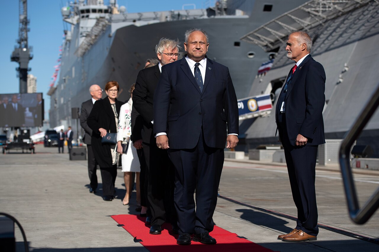 People line up on a red carpet outside a Navy ship.