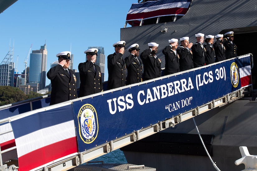 Sailors stand on a ramp and salute during a ship's commissioning ceremony.