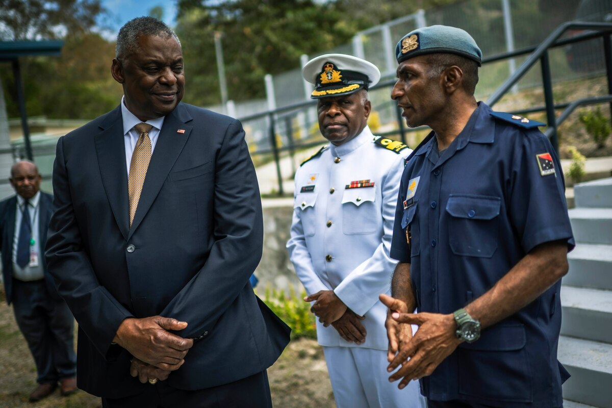 Three men talk while standing next to each other.