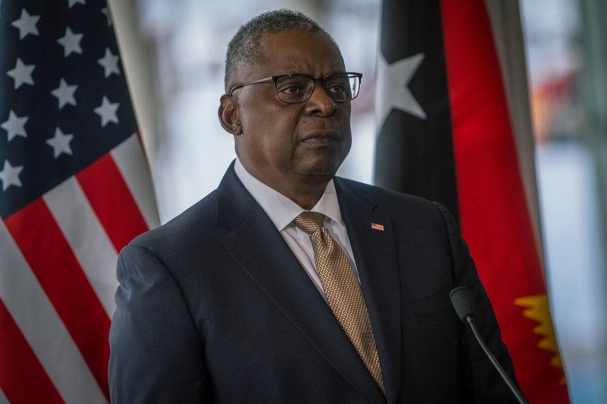 A man speaks with flags in the background.