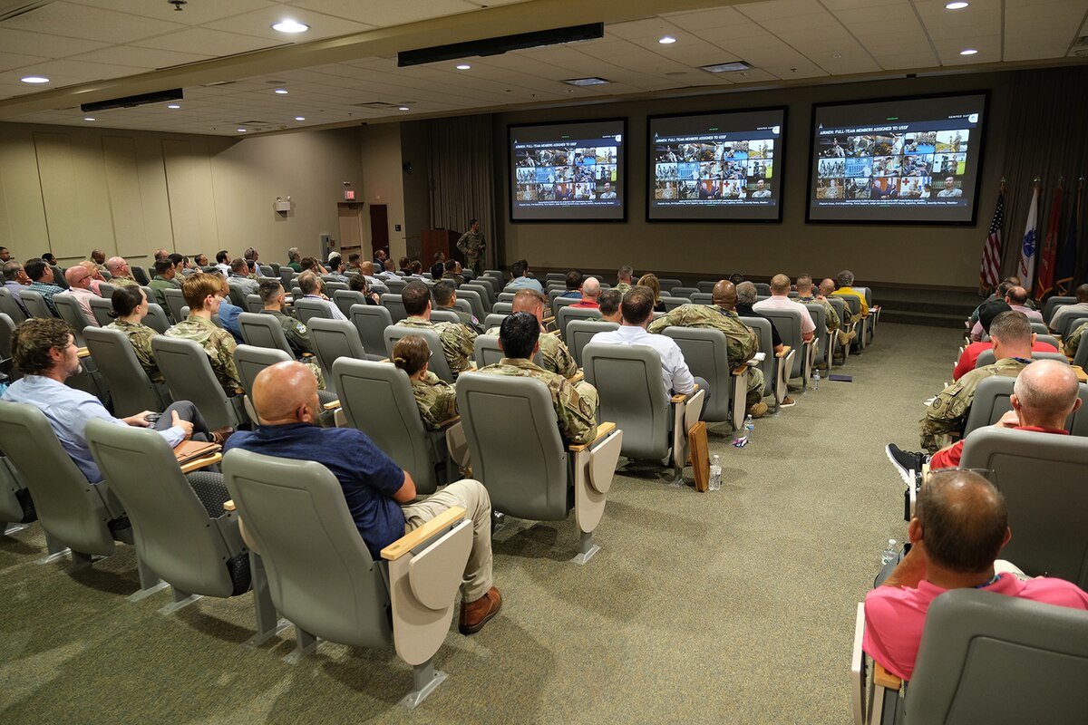 photo of large classroom filled with civilians and military members sitting in chairs with three projector screens