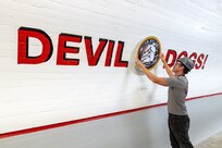 Michael Brown, shipfitter, Shop 11-17, Shipfitters, Forge and Sheetmetal, hangs a sign created by the Shop 11/17 Sign Shop June 16, 2023, while working in the gym area inside the newly refurbished Capt. Patrick M. Rapicault Hall, at Puget Sound Naval Shipyard & Intermediate Maintenance Facility, in Bremerton, Washington. (U.S. Navy photo by Wendy Hallmark)