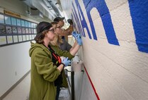 Jeni Brown, Dakota Carver and Matt Grimes, painters, Shop 71, Painters, paint the outline for the word "MARINES!" June 16, 2023 inside Capt. Patrick M. Rapicault Hall, at Puget Sound Naval Shipyard & Intermediate Maintenance Facility, in Bremerton, Washington. (U.S. Navy photo by Wendy Hallmark)