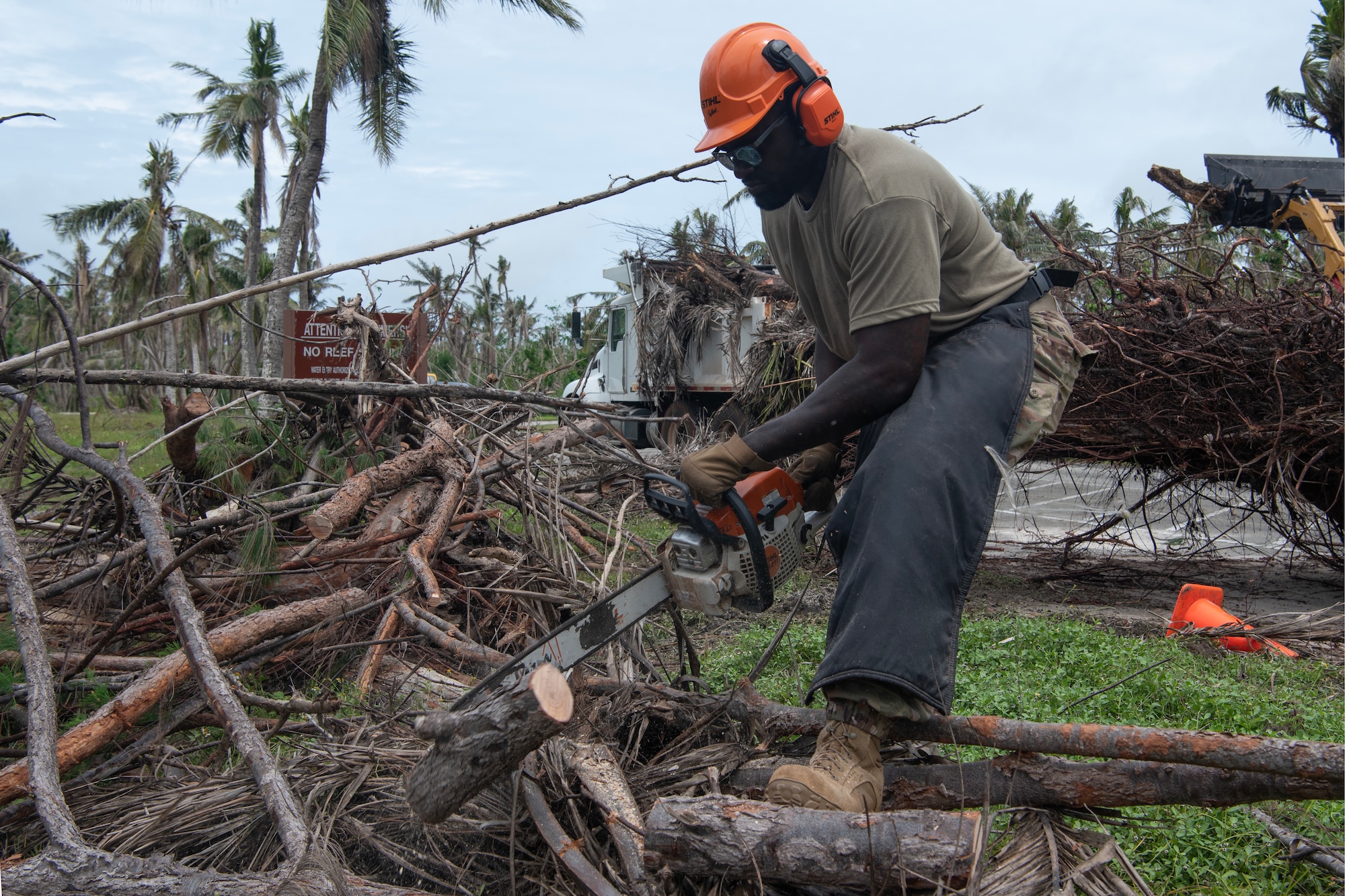 A visiting Airman uses a chainsaw to cut a tree branch.