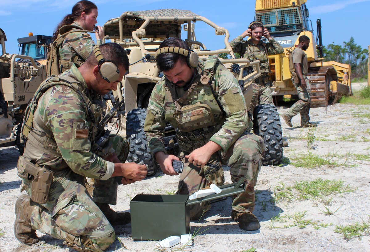 Airmen kneel on the ground loading bullets in magazines
