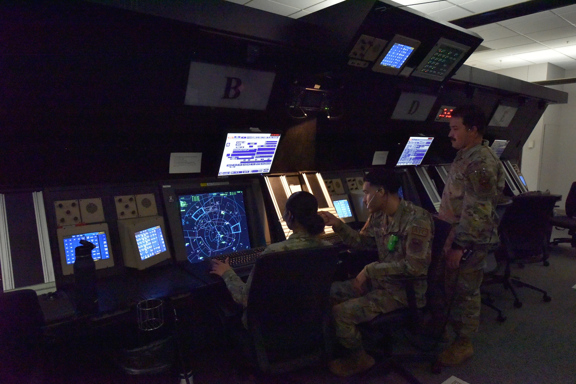 Three Airmen are looking at a radar screen showing the position of aircraft.