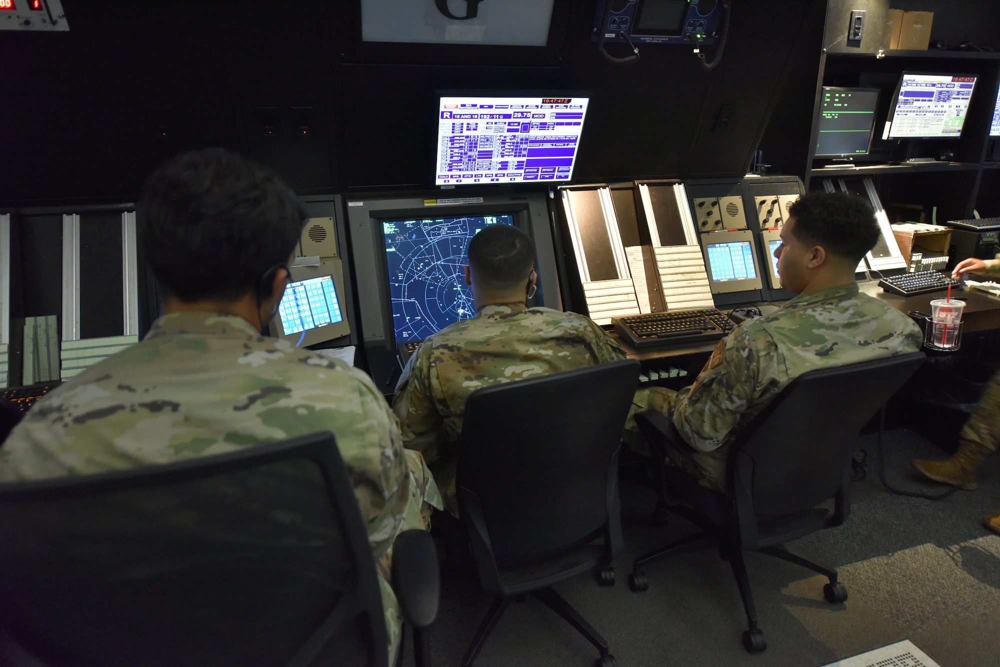 Three Airmen watch a blue radar screen.