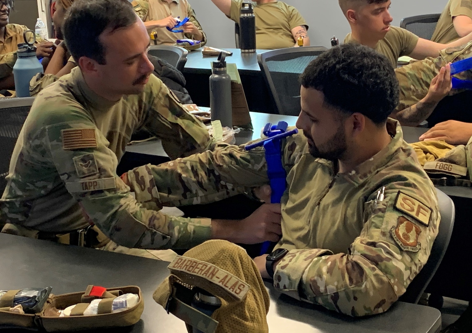 One Airman places a tourniquet around the upper arm of another Airman.