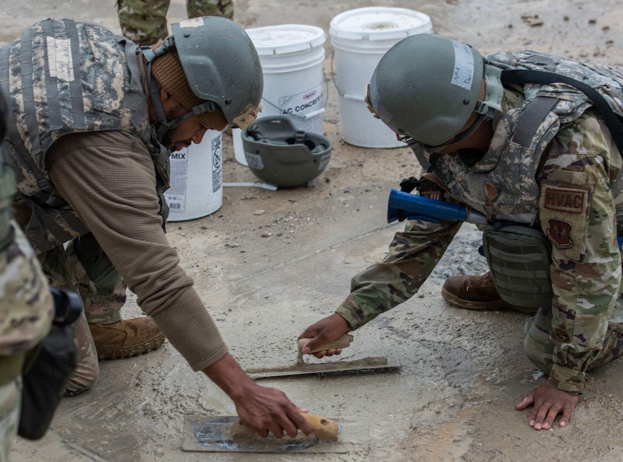 Two Airmen use tools to smooth out concrete