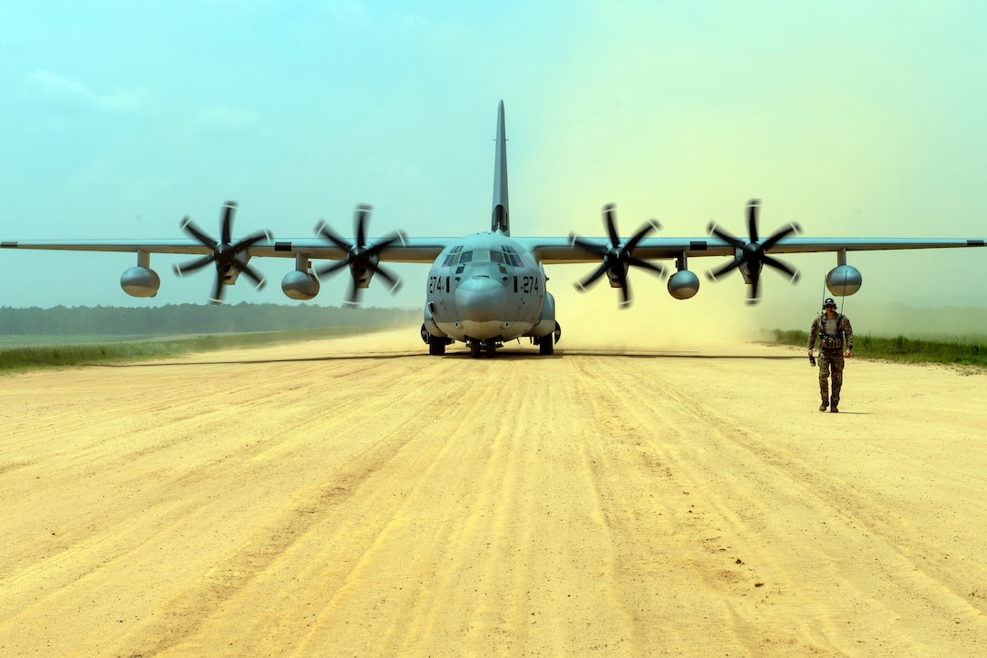 An airman walks in front of a large aircraft.