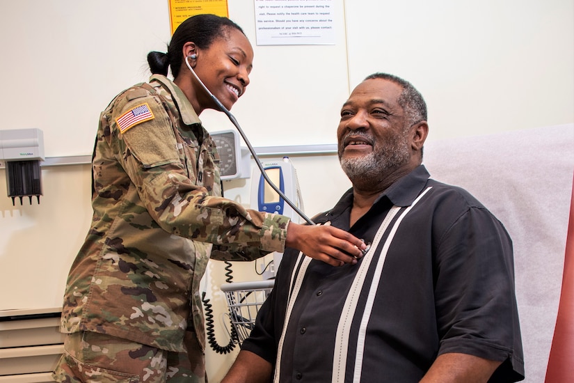 An Army physician examines a seated patient as both smile.