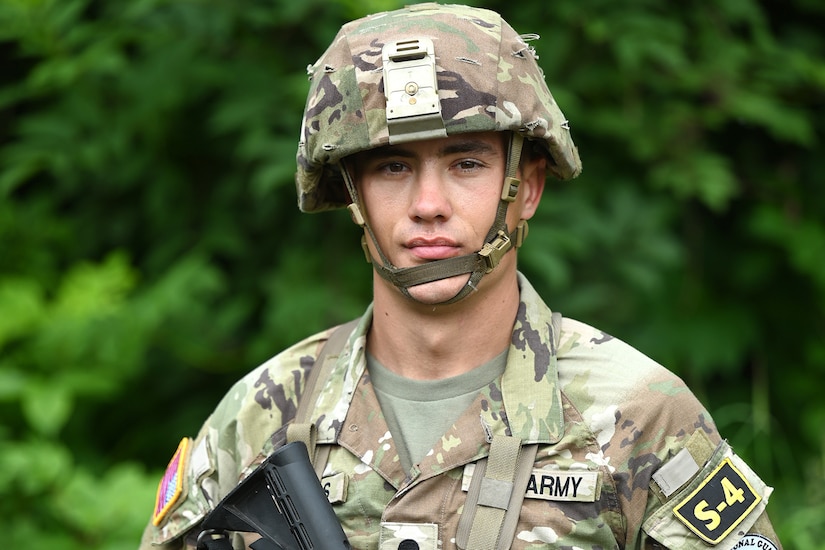 A uniformed soldier poses for a photograph while holding a weapon.