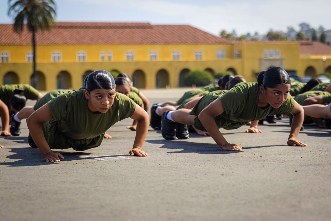 Marines perform pushups in front of a yellow building.