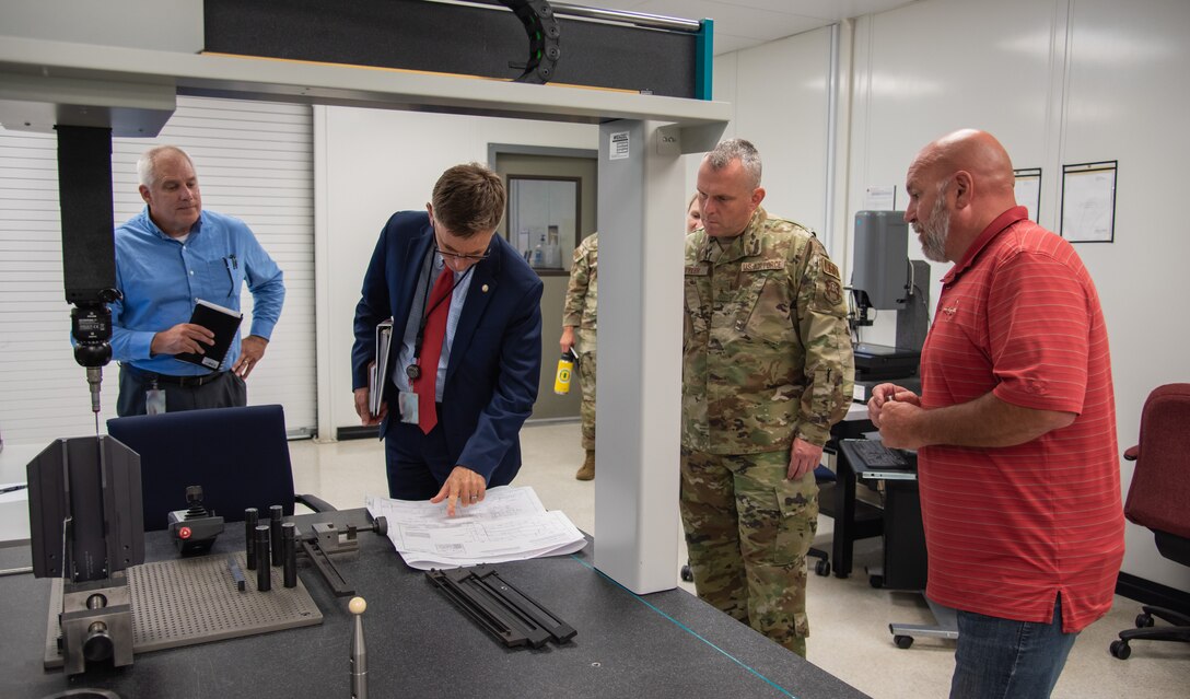 Four men stand in front of a machine. One is in military uniform.