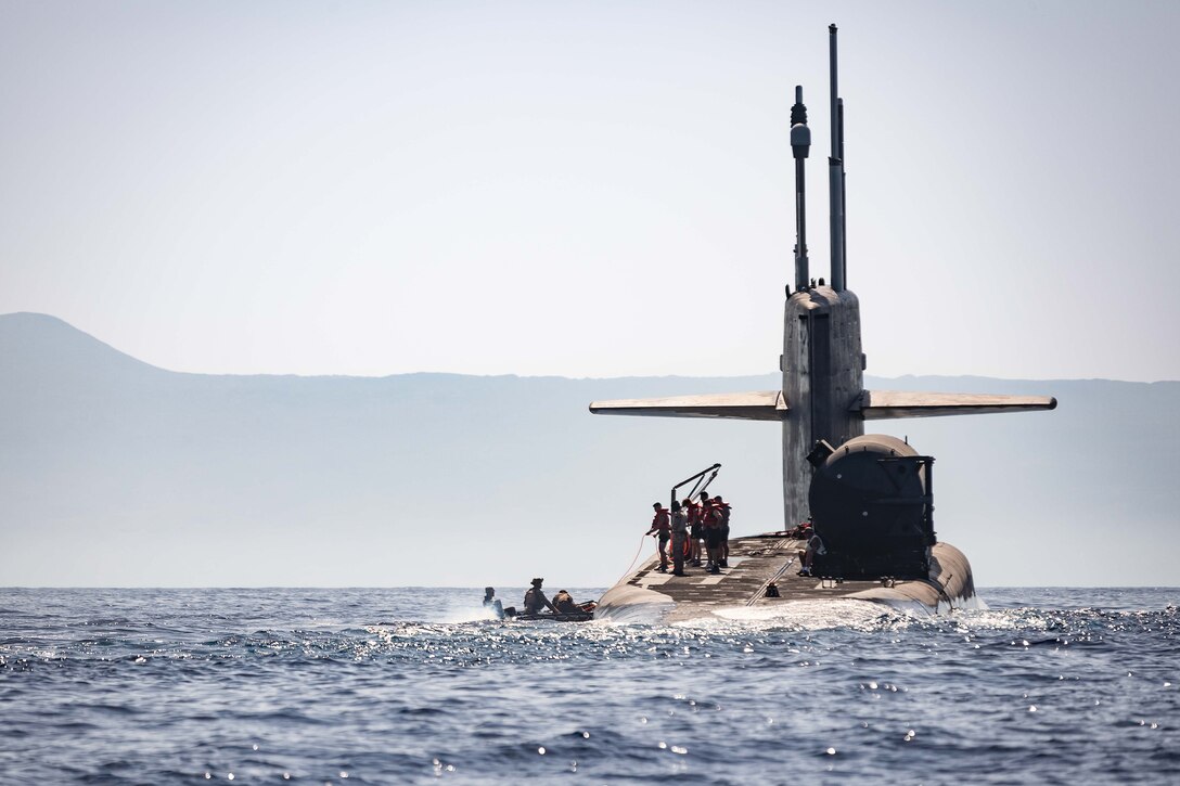 Marines and sailors stand atop a submarine in open water.