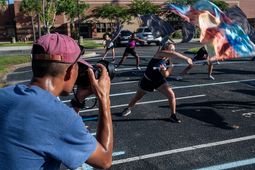 A man takes a photo of a team of people flying flags in unison.