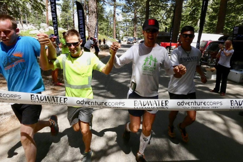 Four men hold hands as they prepare to break and cross finish line tape during a race.