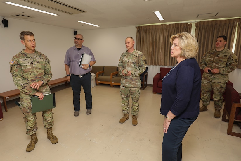 A uniformed service member and a lady wearing business attire look at each other in a room while several others look on.