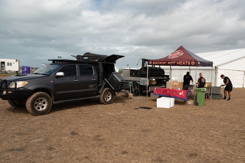 A truck is attached to a trailered barbeque smoker set up next to a tent.