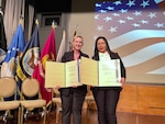 Two women stand on stage holding awards certificates.