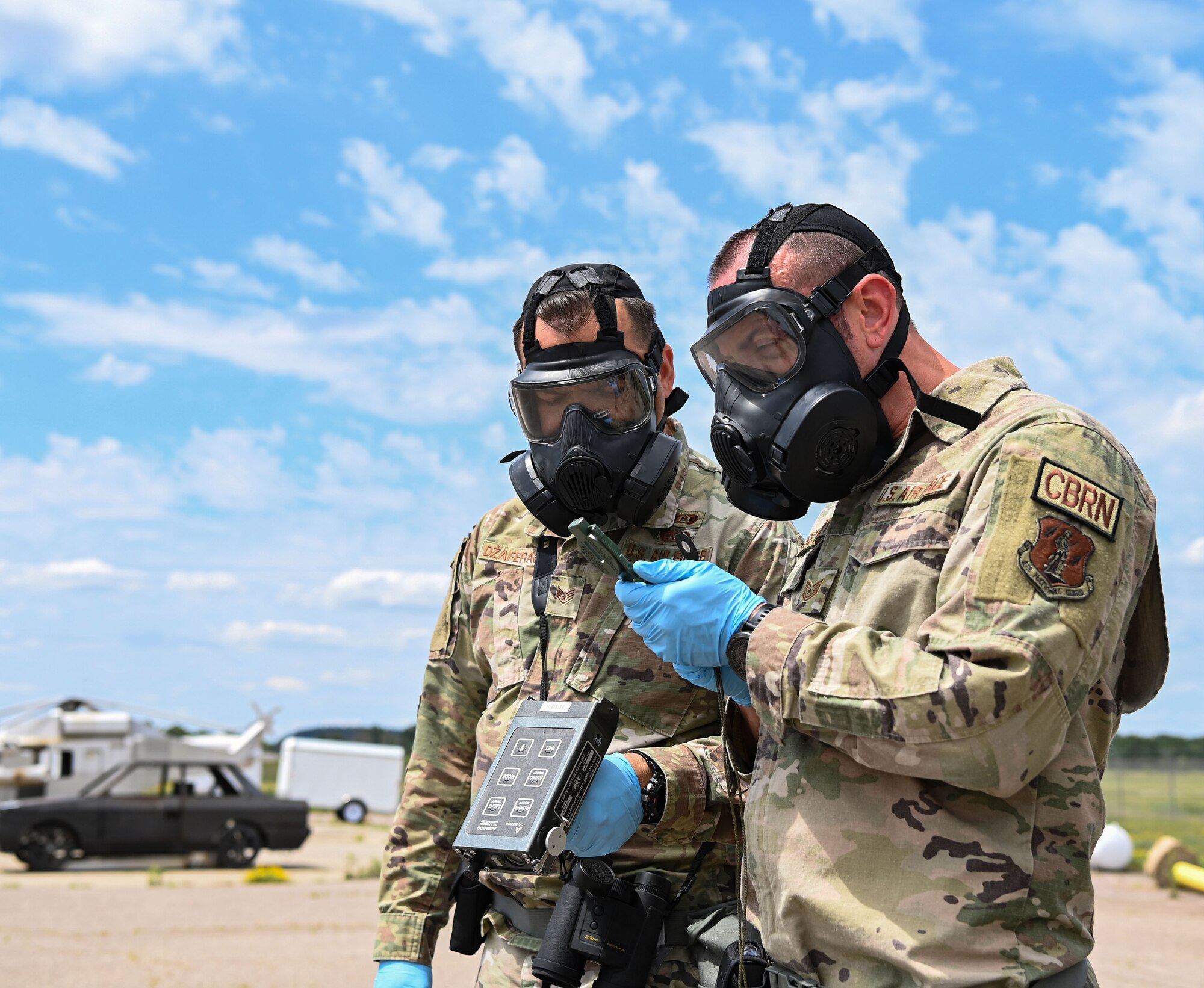 Two airmen in camo wearing gas masks examine a compass