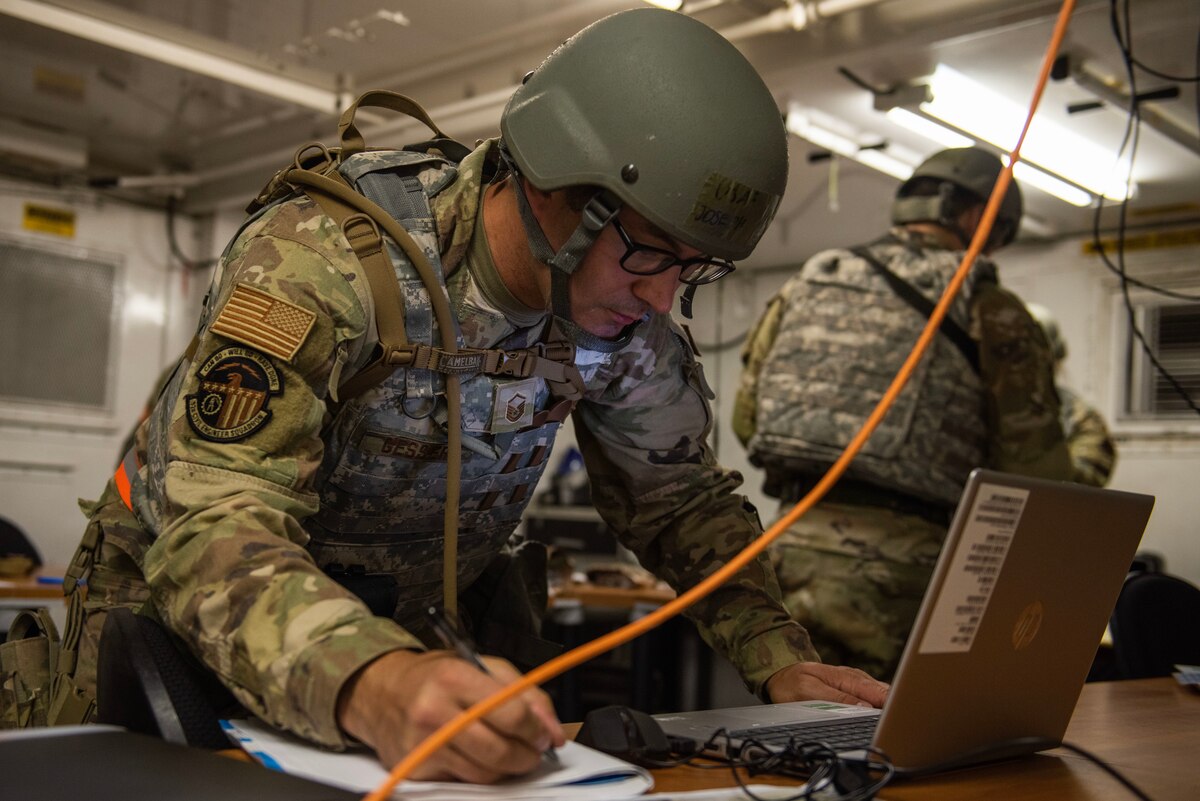 A man uses a computer while writing something down on paper