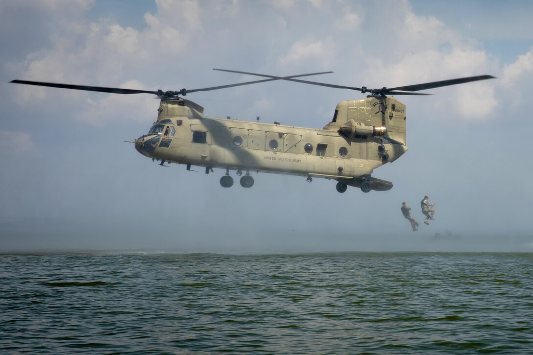 Two soldiers jump from the rear of a CH-47 Chinook helicopter into a lake.
