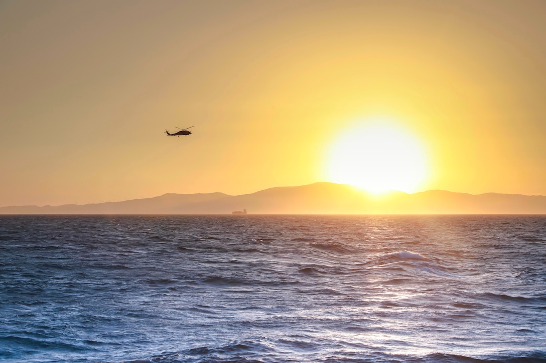 A helicopter flies over the ocean at dusk.