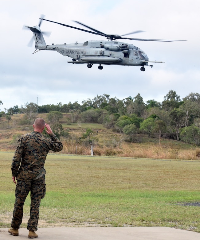 A person in a military uniform salutes as a helicopter lifts off.