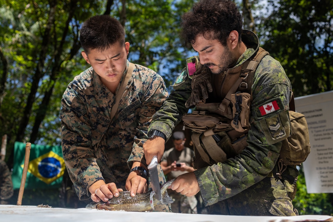 Uniformed service members use a knife to skin a fish.