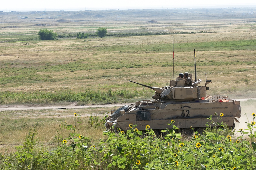 An armored military vehicle crosses a field.