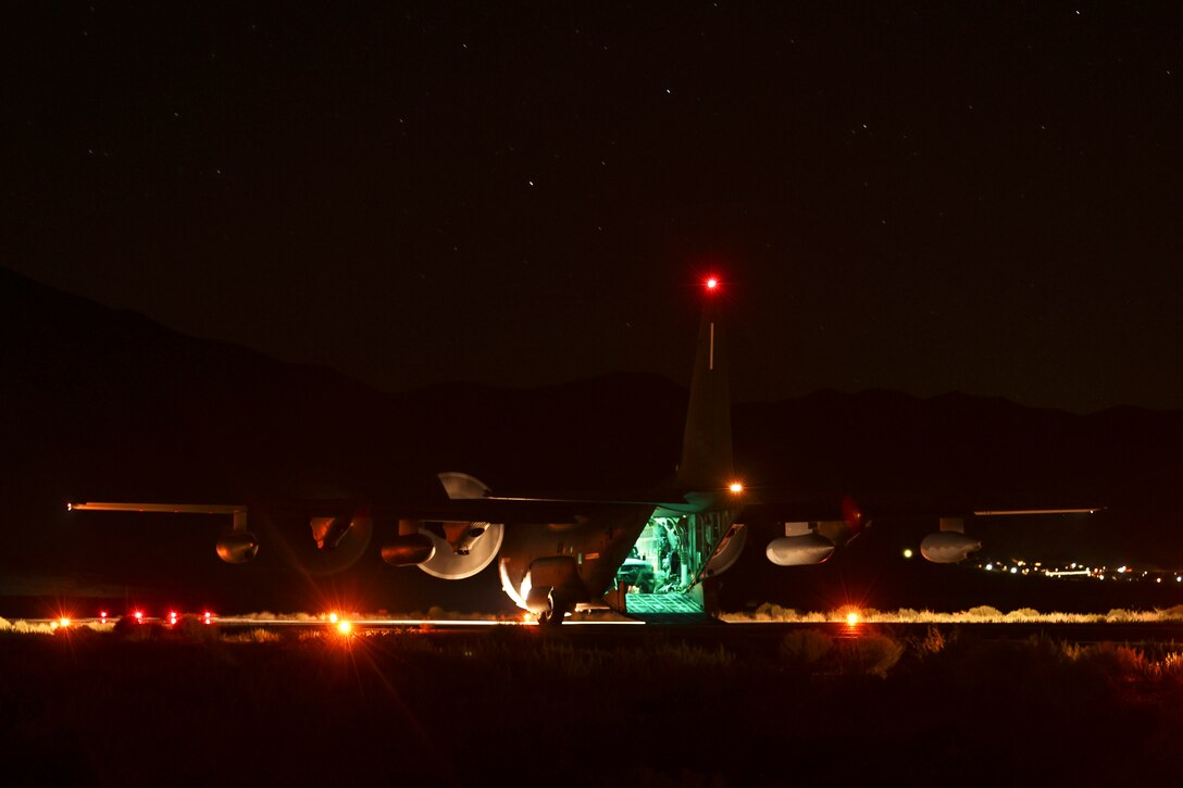 Sailors offload a vehicle from the open doorway of an aircraft parked on a tarmac illuminated by red lights.