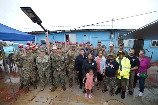 A celebratory pose to commemorate the completion of the final metal roof installation by Task Force RISEUP in Dededo, Guam in response to Typhoon Mawar July 27. Those pictured include representatives of the U.S. Army, U.S. Air Force, U.S. Navy, U.S. federal partners, Guam Governor Lou Leon Guerrero, Dededo Vice Mayor Peter Benevente and RISEUP roof recipients Fely and Gerald Baza with one of their granddaughters.
