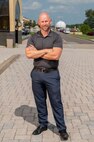 The image depicts a person posing for a portrait outdoors.  They are standing on brick pathway, a road can be seen behind them.