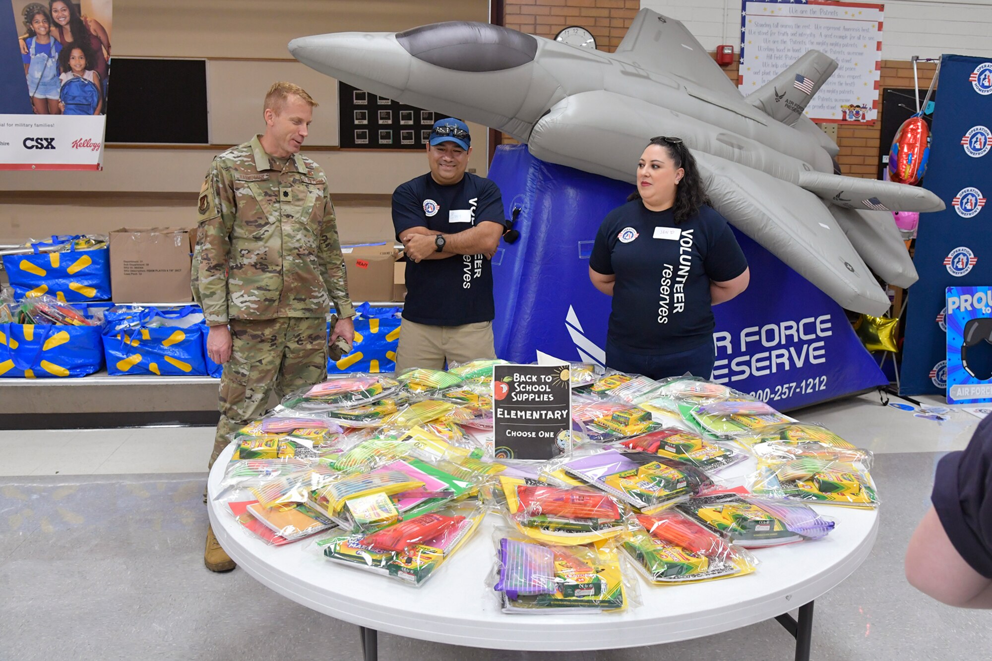 Volunteers stand behind a table filled with school supplies.