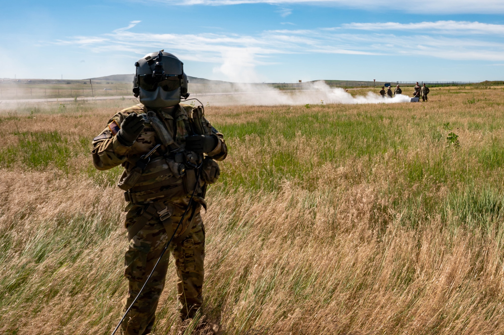 A man stands in a field with people and smoke in the background.