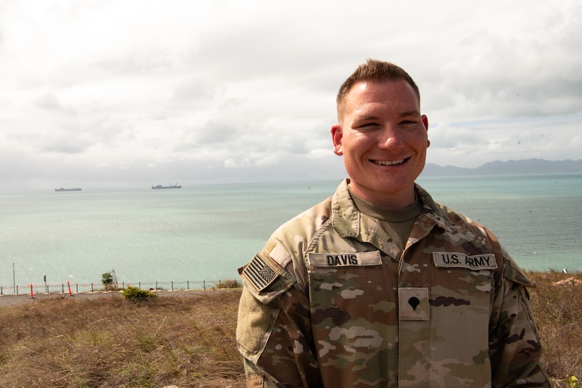 A man in uniform stands on a high overlook with the ocean in the background.