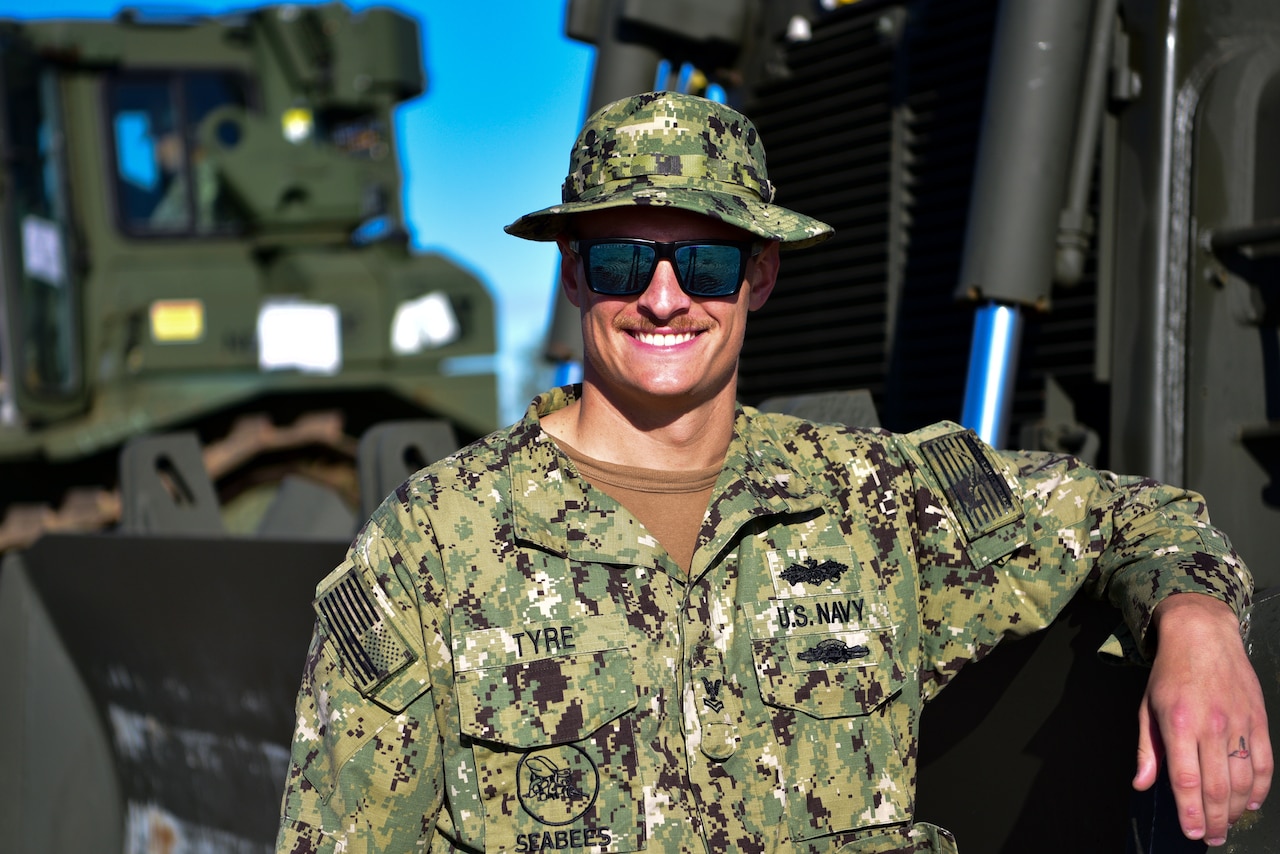 A man in uniform stands next to a bulldozer.