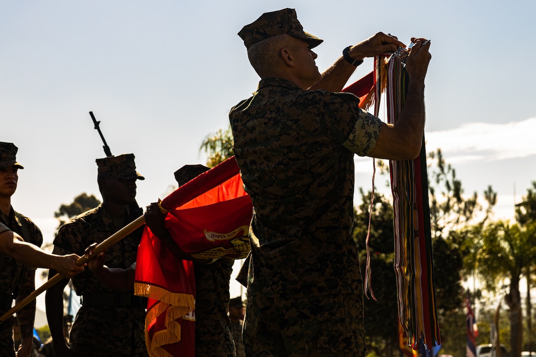 U.S. Marine Corps Brig. Gen. Andrew Niebel, the commanding general of 1st Marine Logistics Group, attaches the Iraq Campaign Streamer to the Marine Corps flag during the 76th Anniversary Battle Colors Rededication Ceremony of 1st MLG at Camp Pendleton, California, July 27, 2023. 1st MLG has more than 8,500 Marines and Sailors serving in various capacities such as transportation and distribution, ammunition and fuel support, supplies and materiel handling, medical and dental services, general engineering, maintenance operations, food services, landing support, and various administrative functions. For 76 years 1st MLG Marines and Sailors have proven themselves, in both peacetime and combat, across the range of military operations from the wars in Korea and Vietnam to the deserts of Kuwait and Somalia and throughout the most recent conflicts in Iraq, Afghanistan, and Syria. Today, 1st MLG stands ready to provide combat service support to I Marine Expeditionary Force in any crisis or contingency and continues to firmly uphold the ‘Victory Through Logistics’ motto.