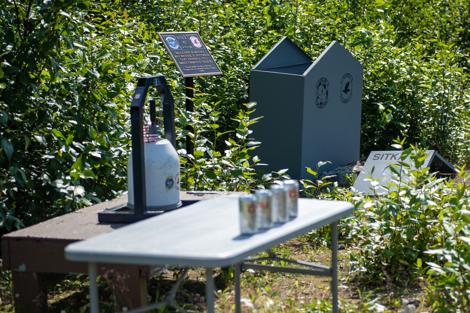 A bell and a table with four alcoholic beverages are seen next to the memorial for the crash site of “Sitka 43”.