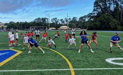 lines of about 25 kids and coaches exercise on a football field