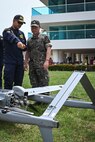 Photos of NITAS members from Colombia and the Republic of Korea discuss the Aerosonde MK4.7 Hybrid Quad unmanned aerial vehicle during demonstration of at the Club Naval Castillogrande during UNITAS LXIV, July 16, 2023.